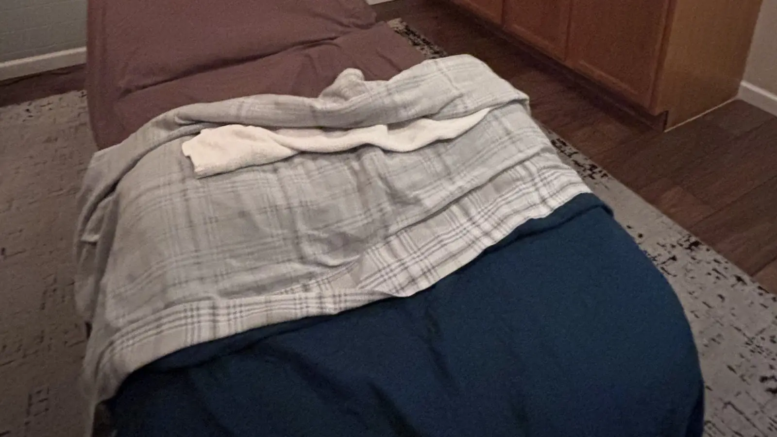 The foot of a treatment table dressed in a plaid blanket and deep blue drape over a patterned rug