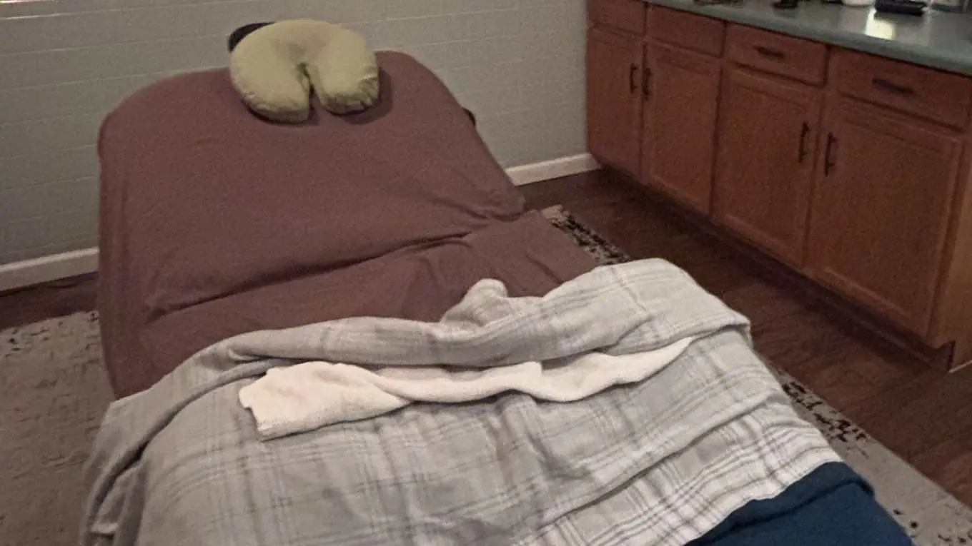 The head of a plum-sheeted treatment table with a green face cradle and a soft plaid blanket