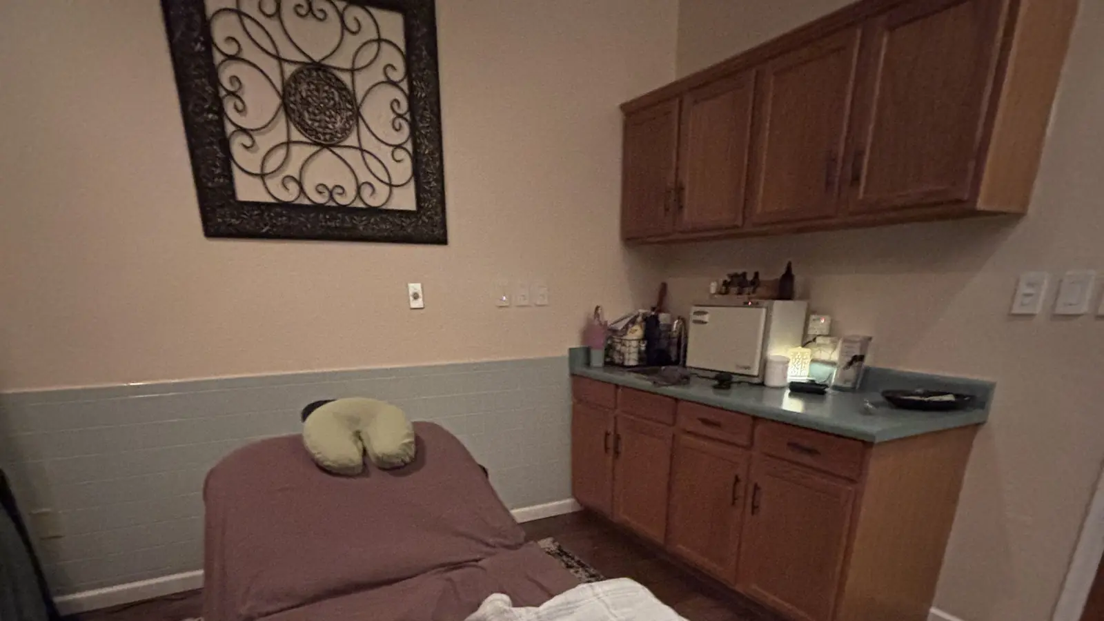 The Fluid Energies treatment room: plum-sheeted table, scrollwork wall panel, sage wainscot and wood cabinets